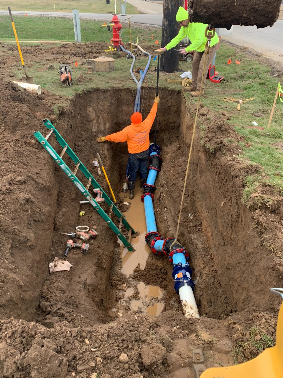 Workers installing underground water pipes in trench.